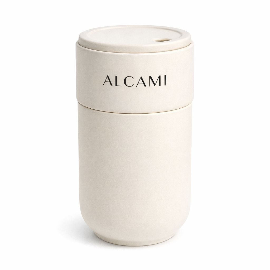 The Alcami Cream Tumbler is a white, reusable travel mug with a lid and "ALCAMI" printed on the upper half. Crafted from ceramic, this tumbler features a minimalistic, modern design—an ideal piece of minimalist drinkware displayed against a plain white background.